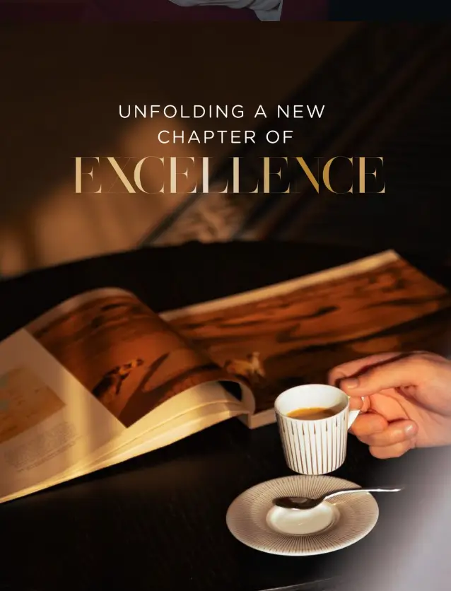 Gold lettering reading Unfolding A New Chapter Of Excellence over a coffee table and open book